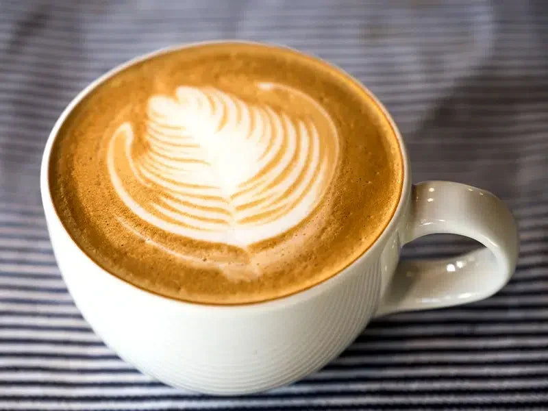 Taza de café con diseño de latte art en la superficie con espuma de leche.