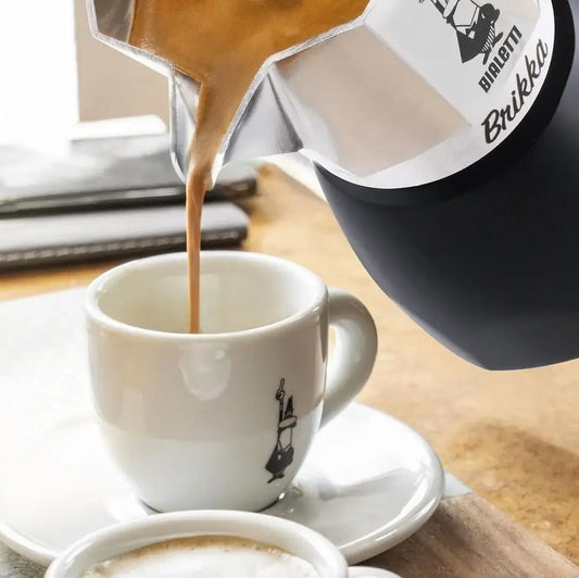 Cafetera Bialetti Brikka sirviendo espresso con crema en taza.
