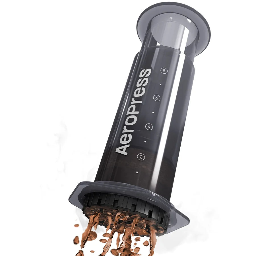 Prensa de café negra AeroPress XL con tapa abierta y café molido cayendo