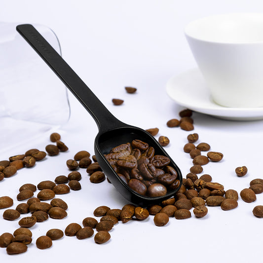 Cuchara de café negra con granos de café en la pala y mango largo