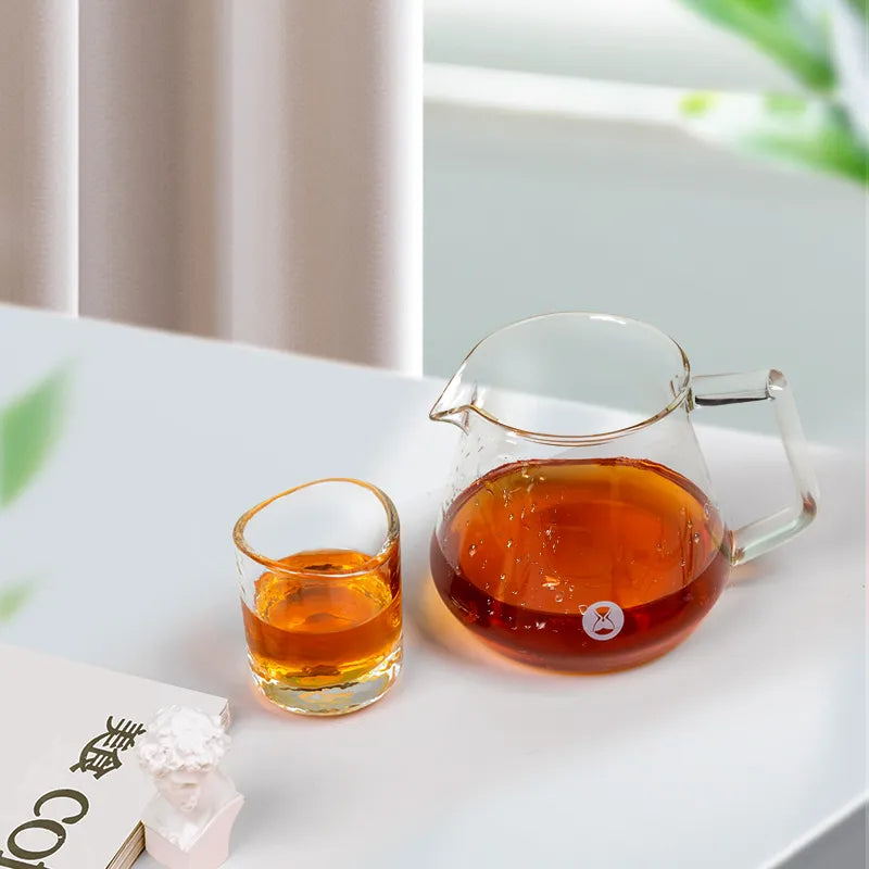 Jarra de café transparente Timemore con asa, con líquido ámbar, y vaso pequeño