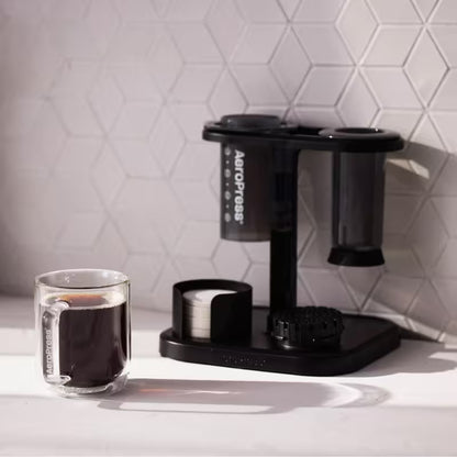 Soporte organizador negro para Aeropress con recipientes cilíndricos y taza sobre base